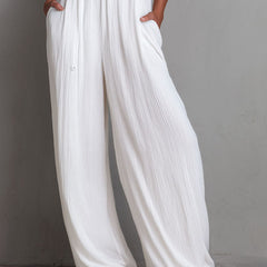 White pleated halter neck wide-leg resort jumpsuit for women, featuring stylish pants with a relaxed fit and elegant design.