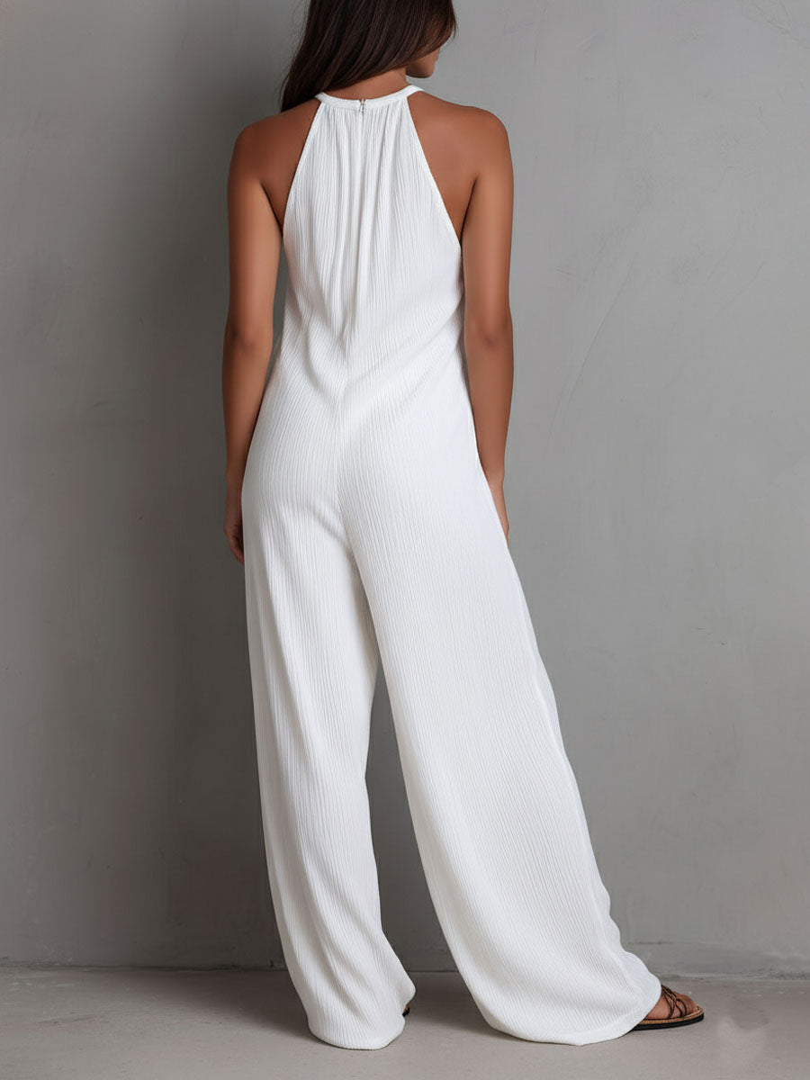 White pleated halter neck wide-leg resort jumpsuit for women, stylish pants with flowing fabric and halter neckline.