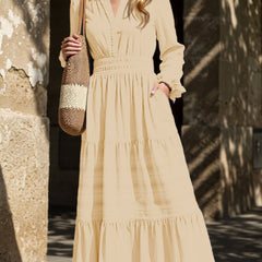 White V-neck pleated waist tiered long-sleeved dress with a flowing silhouette, styled with a soft beige background.