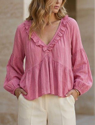 Pink women's summer blouse with V-neck, long sleeves, and ruffle details, made from denim fabric.